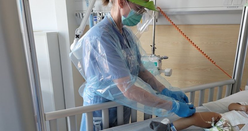 Vårdpersonal ger infusion till ett spädbarn i en sjukhussäng. Foto.